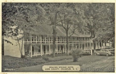 Vintage postcard of the Healing Springs Hotel in Crumpler, North Carolina, a two-story building with a wrap-around porch and cars parked in front, reflecting the history of Healing Springs.
