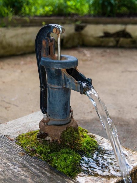 An old metal water pump from the history of healing springs with water flowing from the spout onto a mossy stone base.