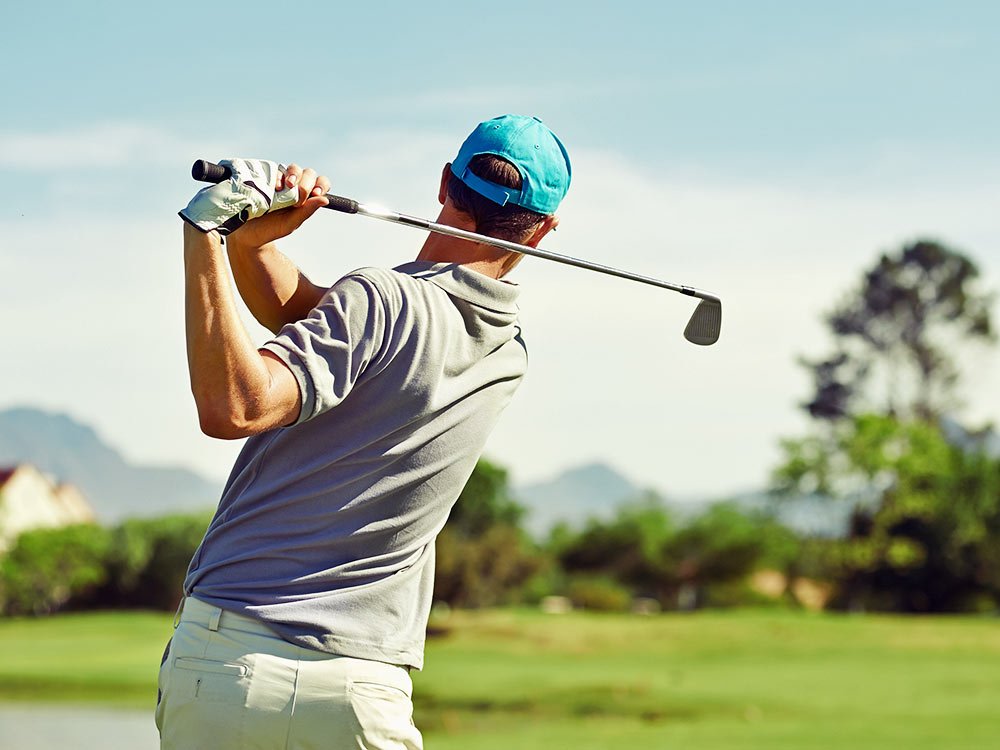 A golfer wearing a cap follows through on a swing at a golf course, one of the many things to do in Ashe County NC.