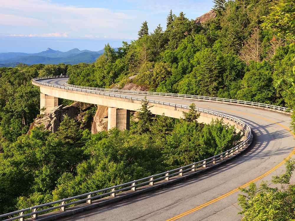 The Linn Cove Viaduct curves along a mountain covered in dense forest, a scenic highlight among things to do in Ashe County NC, with distant blue mountains in the background.