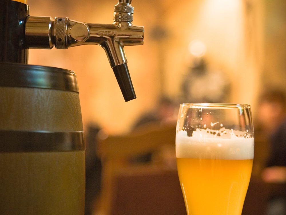 A glass of beer with foam sits next to a beer tap handle at one of the things to do in Ashe County NC.