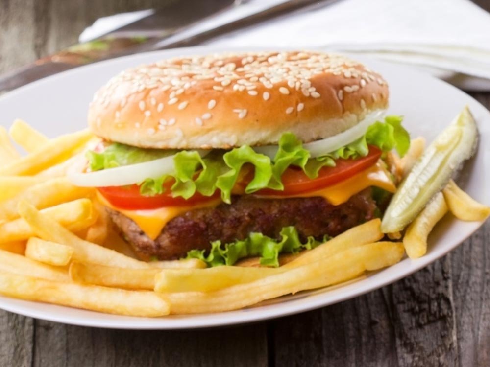 A cheeseburger with lettuce, tomato, and onion on a sesame seed bun, served with fries and a pickle spear, the perfect meal after things to do in Ashe County NC.