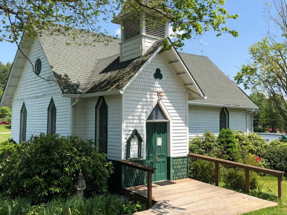 A small white church with a green door, a shingled roof, and a wooden ramp leading to the entrance, representing the many things to do in Ashe County NC.